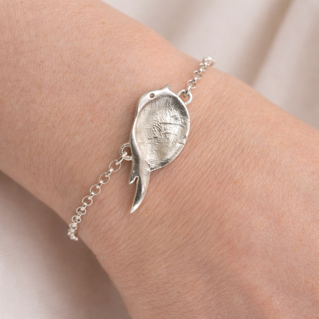 Silver bracelet with a bird shaped charm with a fingerprint on it.