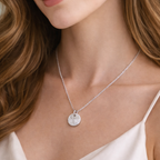 Close-up of a woman wearing a silver necklace with a round fingerprint pendant.
