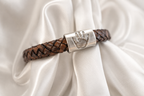 silver charm with a handprint on it on a brown leather bracelet