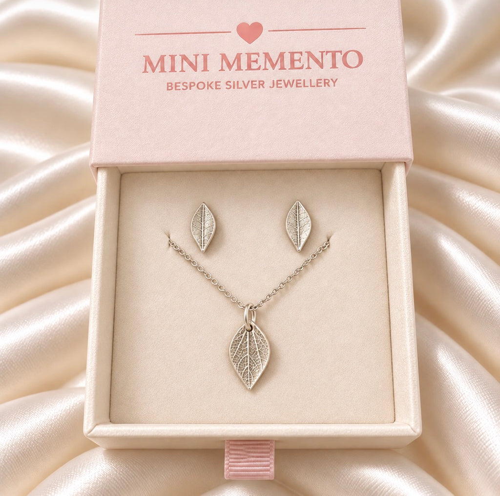A silver leaf pendant necklace and matching stud earrings displayed in a light pink jewellery box. Made by Mini Memento