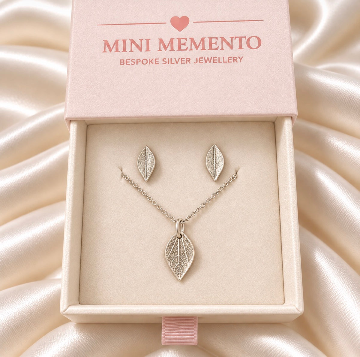 A silver leaf pendant necklace and matching stud earrings displayed in a light pink jewellery box. Made by Mini Memento
